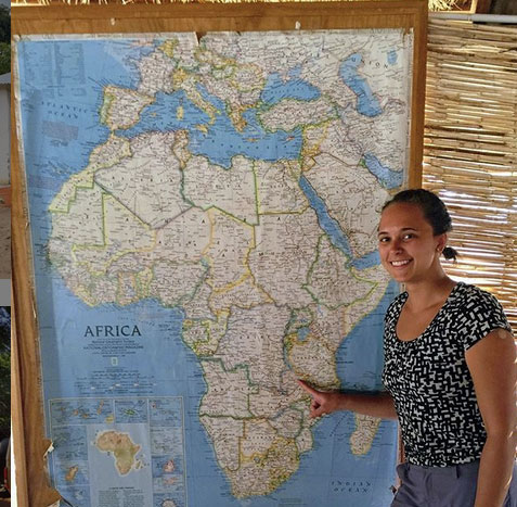 Aubrey stands by a map of Africa, pointing to Zambia
