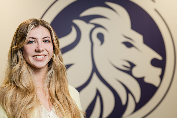 Grace Stolberg standing in front of the logo for O'Keefe Stevens Advisory