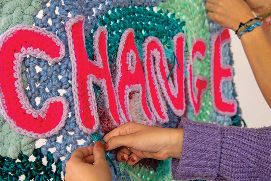 two students knitting the word "change" from yarn