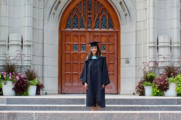 Gabriela Pandya posing in commencement garb in front of Golisano Academic Center