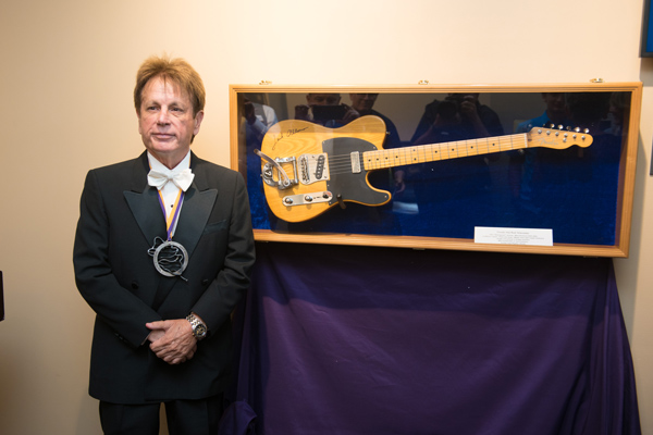 Jack Allocco poses by the new display of his donated guitar in Glazer Music Performance Center