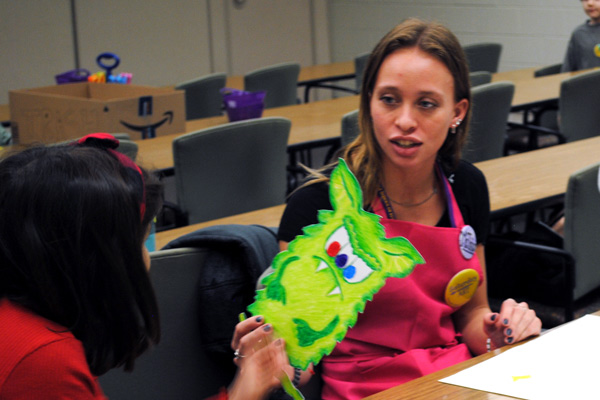 Lizzie Tripp holds artwork of a green monster with three eyes and fangs, talking to a child