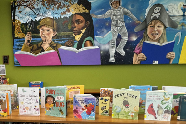 pollinator children's book display at library; colorful images on wall of children reading