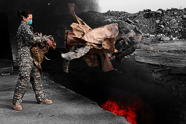 An airman tosses unusable uniforms into a burn pit at Balad Air Base, Iraq