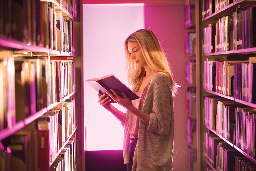 student between to bookshelves reading a book