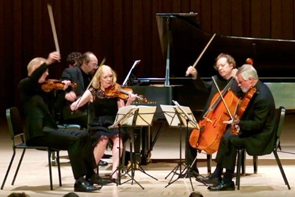 Five string players, bows in the air, and a pianist perform onstage