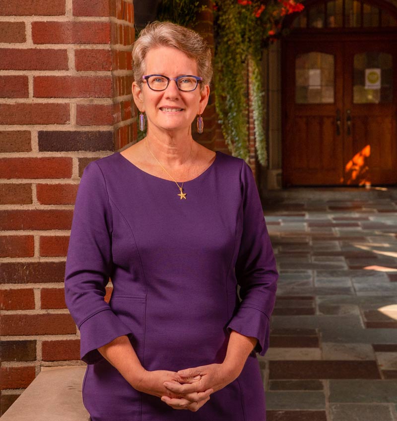 Beth Paul, wearing purple, poses on campus