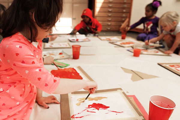 children engrossed in painting at a table, using red paint