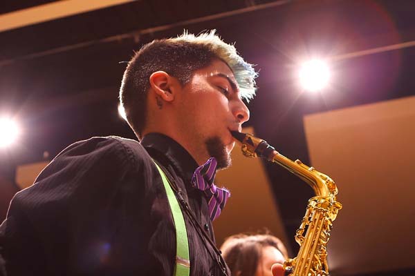 student plays saxophone on stage with bright lights