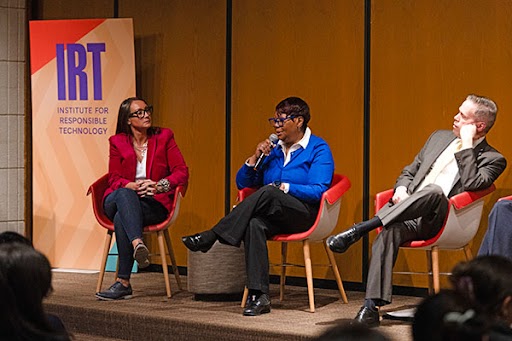 Three people seated onstage, one with a microphone, by an Institute for Responsible Technology sign.
