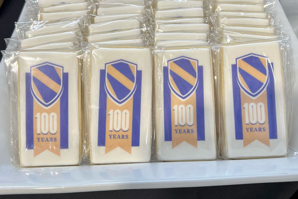 cookies with purple and gold centennial logo, including a shield with a gold sash and "100 years"
