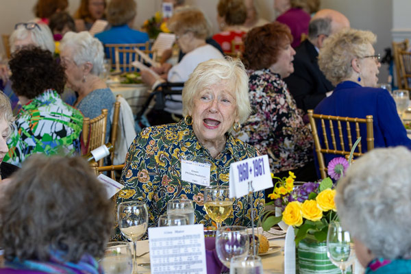 Alumnae sing while seated at Nazareth University’s 51+ club luncheon, holding alma mater lyrics.