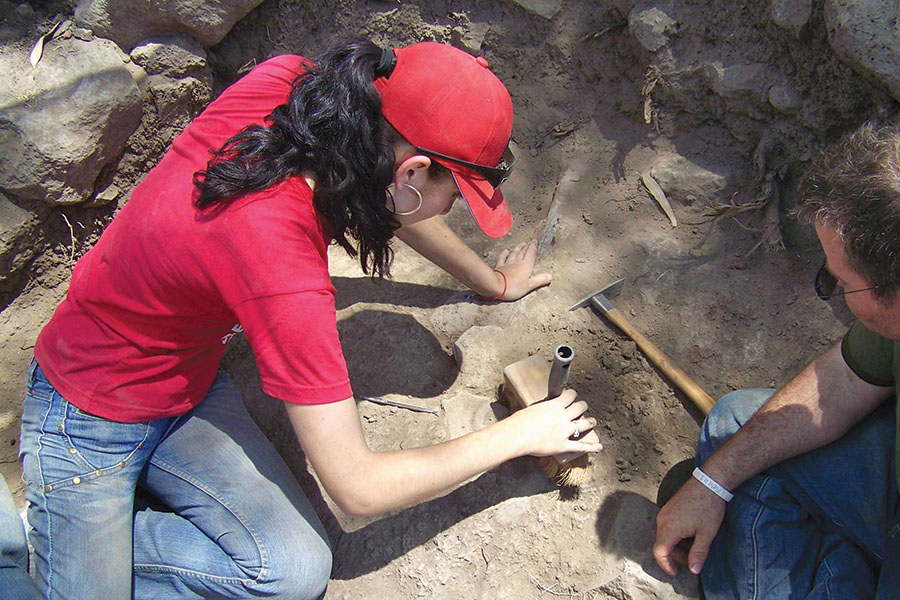 student digging in dirt at archaeological site