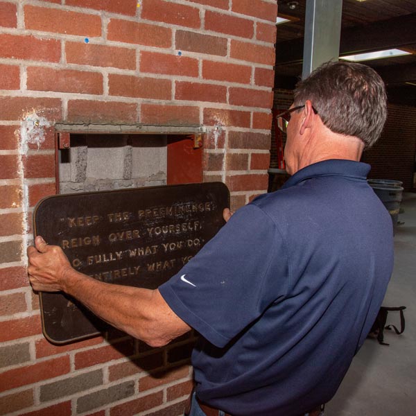 man removing a wall plaque to reveal a time capsule