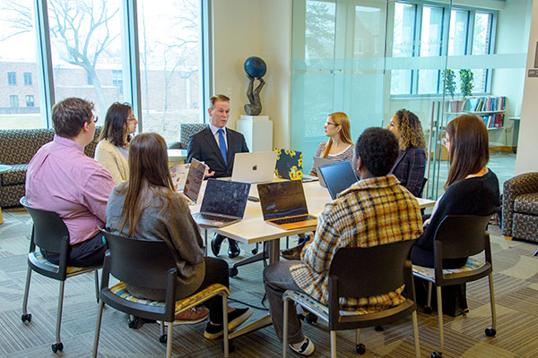 professor and students seated around table with laptops