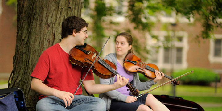 students sitting under a tree playing violins