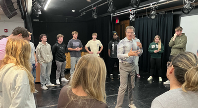 Standing onstage in a circle of Nazareth students, Keith Smith leads an improv workshop.