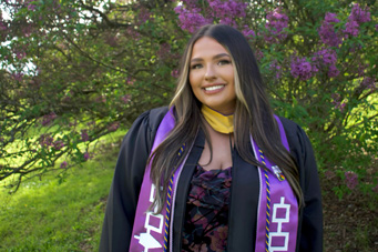 Karlee Cousins poses in graduation cap and gown with a purple stole