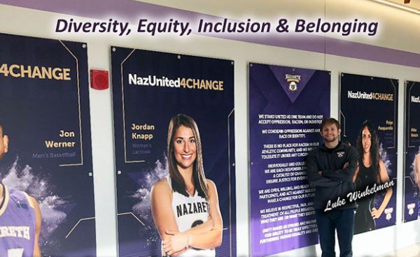 Luke Winkelman stands in front of NazUnited4CHANGE athlete wall display at Golisano Training Center