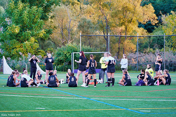 field hockey players sitting on field listening to coach
