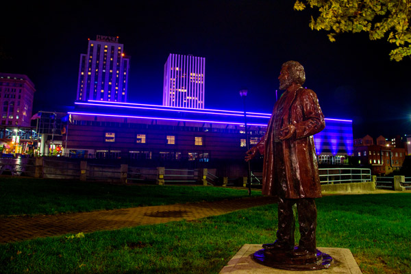 Downtown Rochester buildings lit up in purple, Frederick Douglass statue in foreground