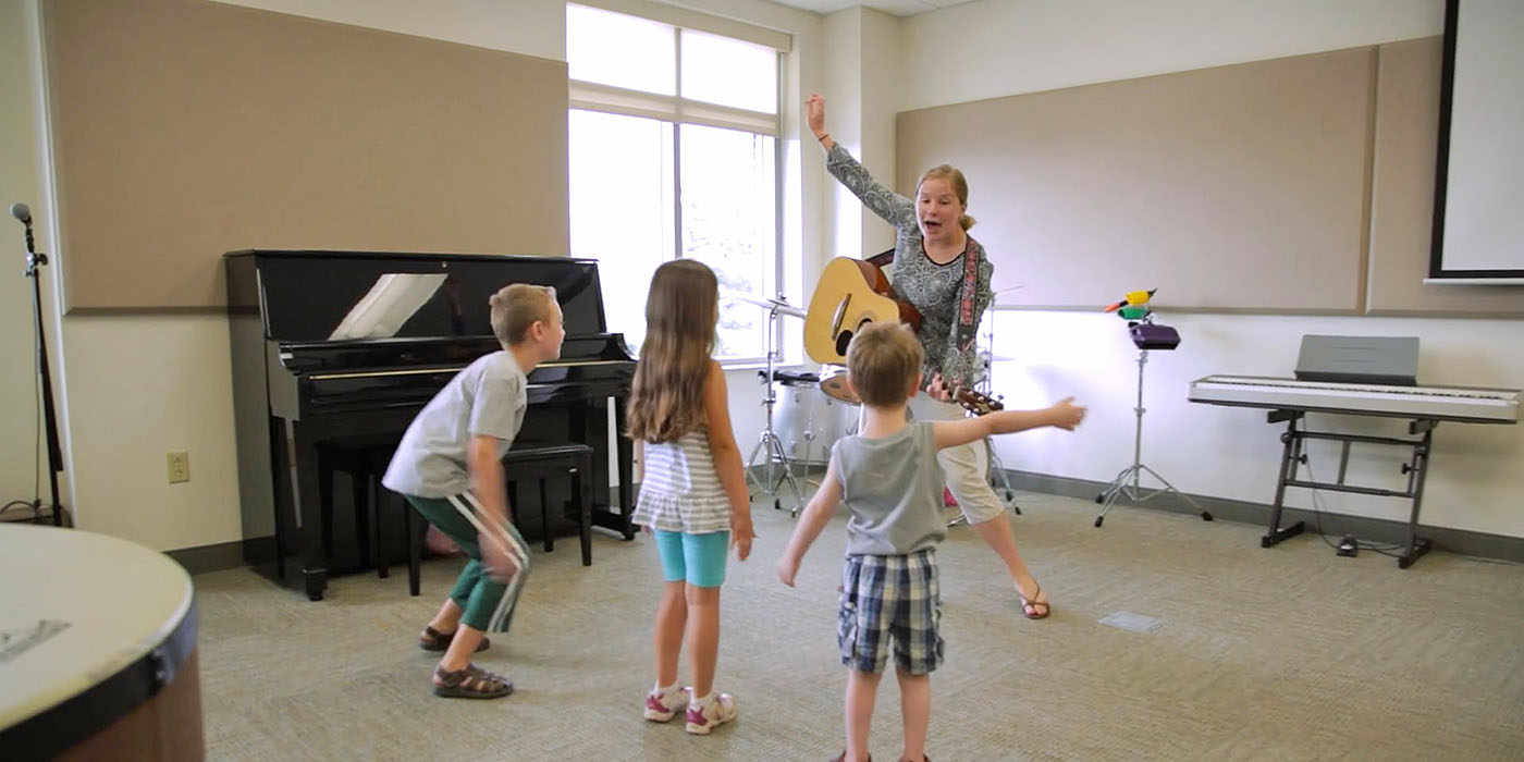 student singing and playing guitar for three children