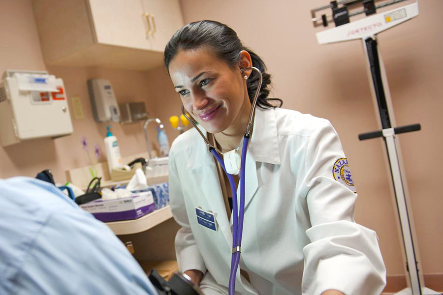 nurse wearing stethoscope in exam room with patient