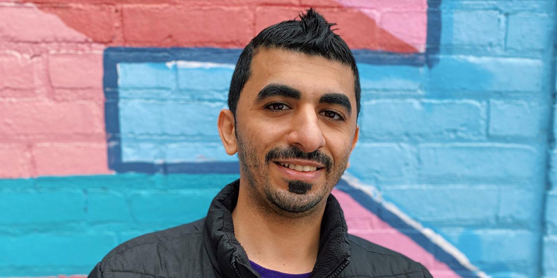 Mustafa Alhabib in front of a brick wall painted in bright colors