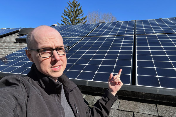 Matt Ferrell with a quizzical expression points to solar panels on a house